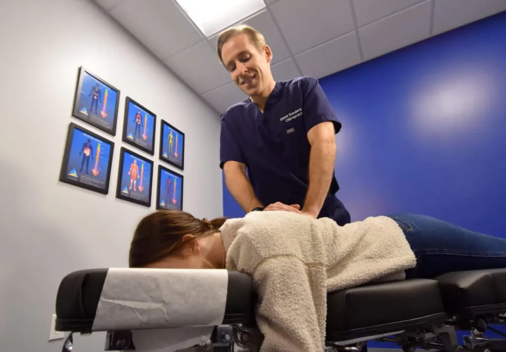 Chiropractor adjusting patient's back on treatment table in clinical room with anatomy charts